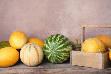 Ripe melons and watermelon on wooden table against color background. Space for text