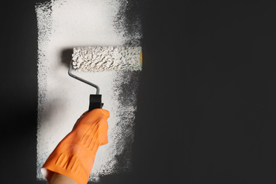 Photo of Woman painting grey wall with white dye, closeup