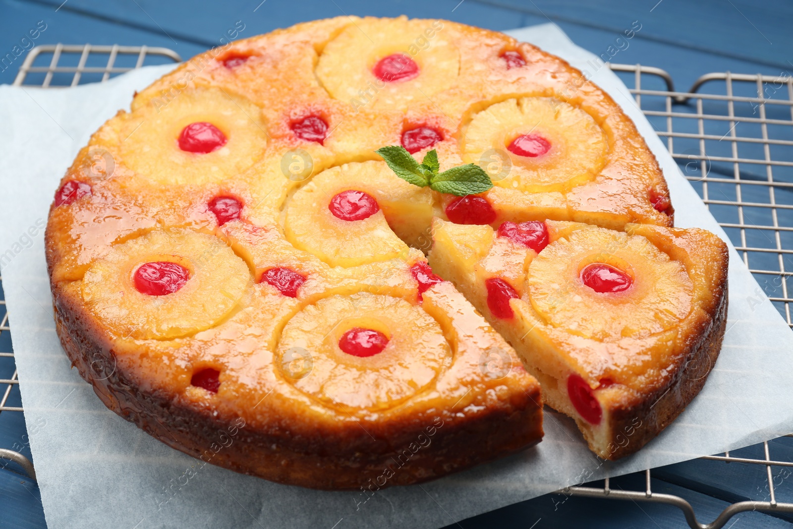 Photo of Delicious cut pineapple pie with cherry on blue table, closeup