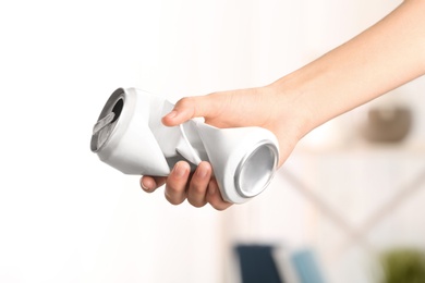 Woman holding crumpled aluminum can on blurred background. Metal waste recycling