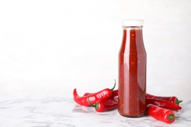 Photo of Glass bottle of hot chili sauce with peppers on table. Space for text