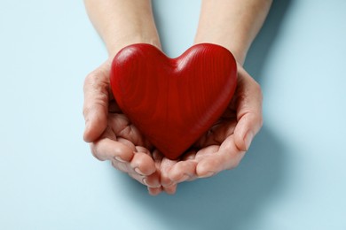 Photo of Elderly woman holding red heart in hands on light blue background, closeup
