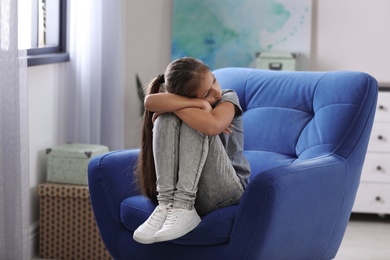 Depressed preteen girl sitting in armchair at home