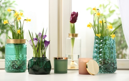 Photo of Different beautiful spring flowers and candles on window sill