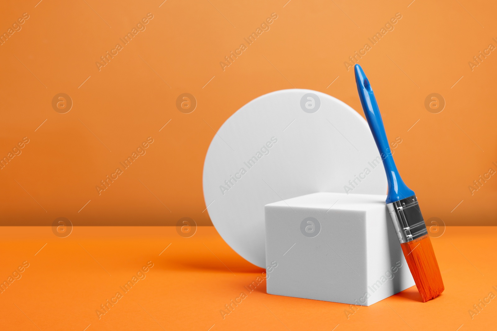 Photo of Scene with podium for product presentation. Figures of different geometric shapes and paint brush on orange background, space for text