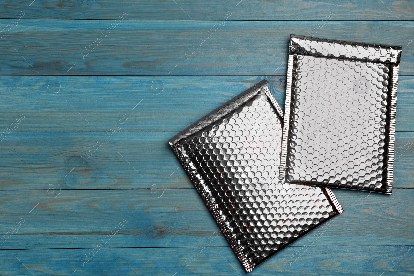 Photo of Two padded envelopes with bubble wrap on light blue wooden background, flat lay. Space for text