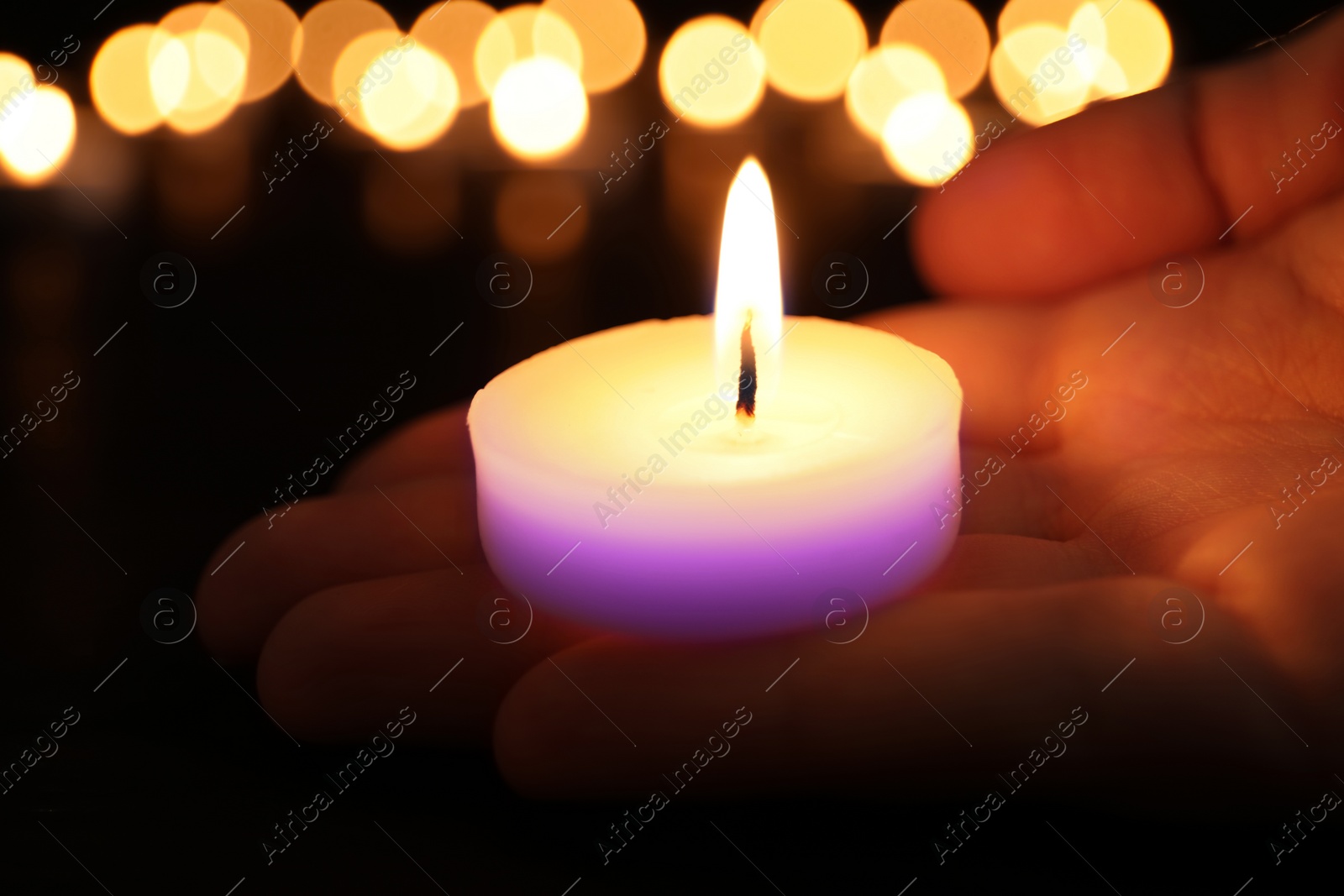 Image of Woman holding burning violet candle in darkness, closeup. Funeral attributes