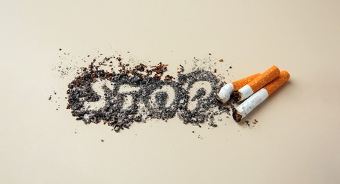 Word Stop made of cigarette ash and stubs on beige background. Quitting smoking concept