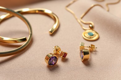 Photo of Elegant earrings, bracelets and necklace on beige cloth, closeup