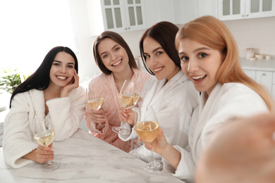 Photo of Beautiful young ladies with wine taking selfie in kitchen at pamper party. Women's Day