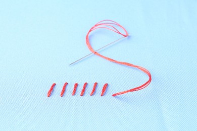 Photo of Sewing needle with thread and stitches on light blue cloth, closeup