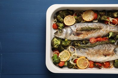 Photo of Delicious fish with vegetables and lemon in baking dish on blue wooden table, top view. Space for text