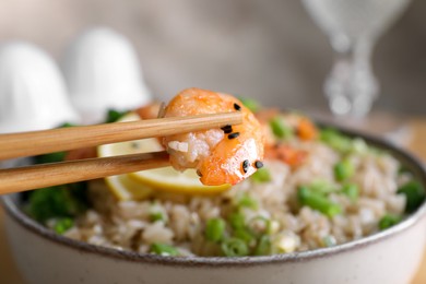 Photo of Chopsticks with shrimp above tasty rice and vegetables, closeup