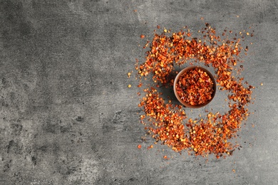 Photo of Bowl with chili pepper flakes on grey background, top view