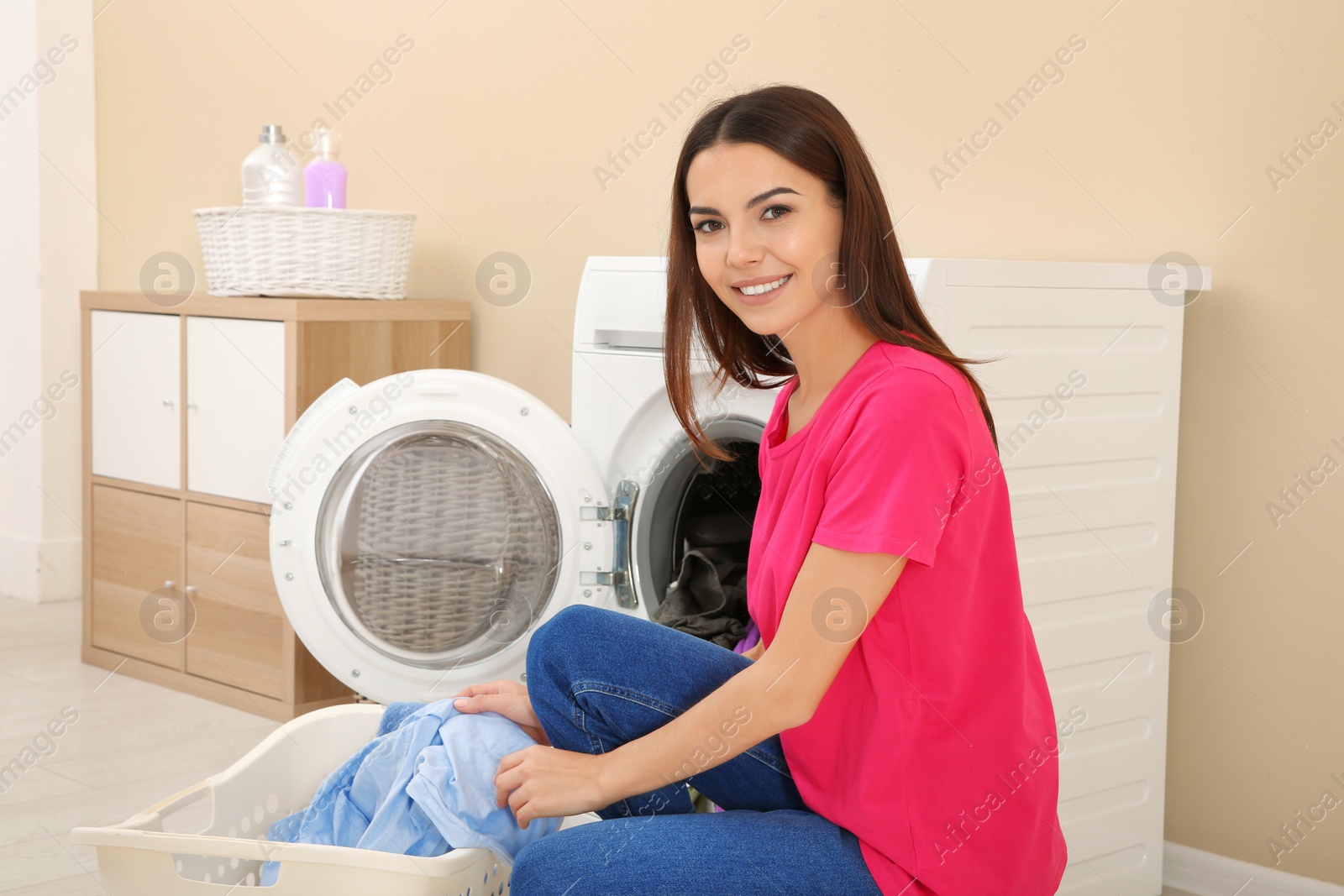 Photo of Young woman taking laundry out of washing machine at home
