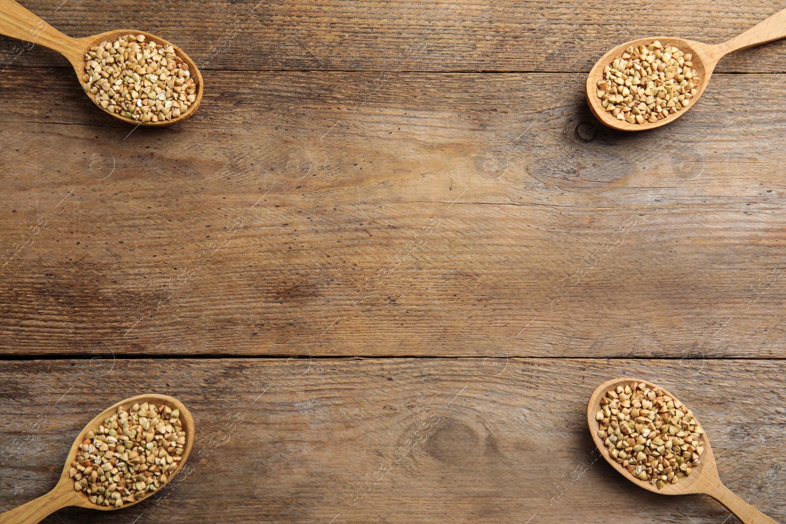 Photo of Uncooked green buckwheat grains in spoons on wooden table, flat lay. Space for text