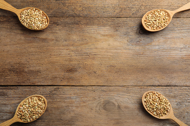 Uncooked green buckwheat grains in spoons on wooden table, flat lay. Space for text