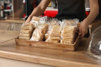 Photo of Worker holding tray with delicious pastries at desk, closeup
