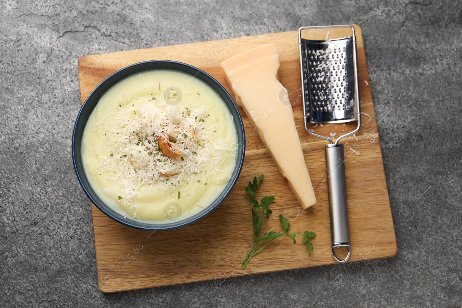 Photo of Delicious cream soup with parmesan cheese and croutons in bowl on grey table, top view