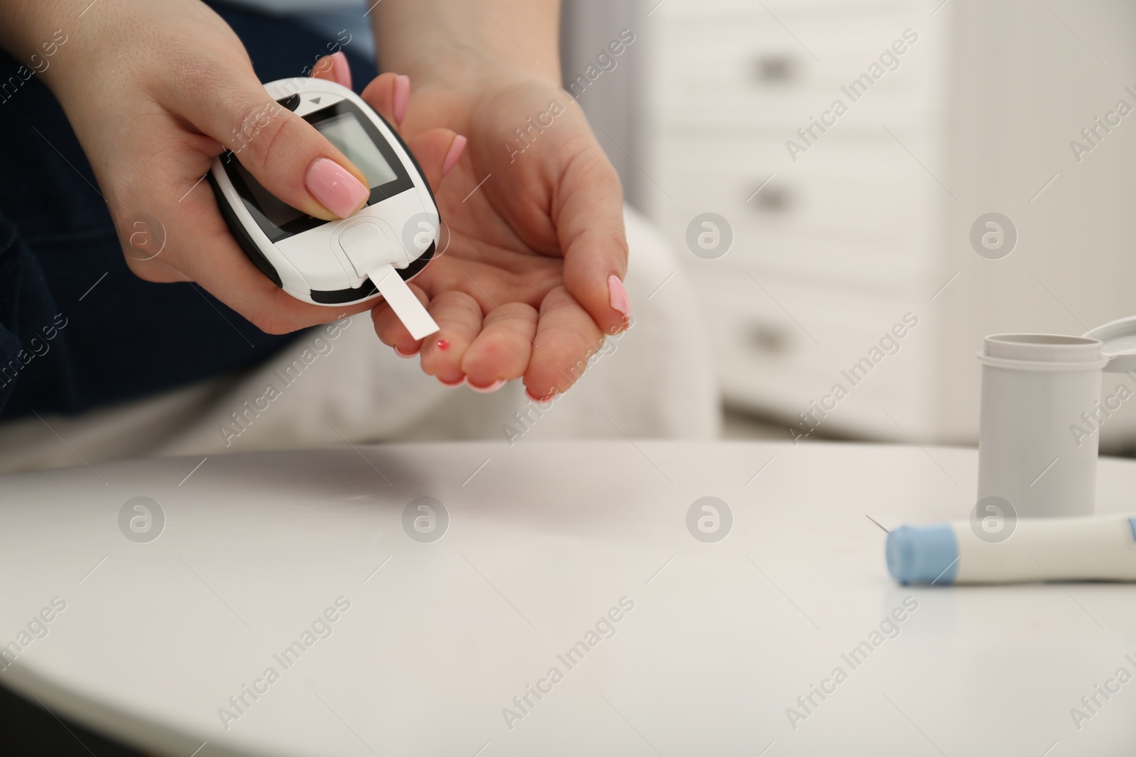 Photo of Diabetes. Woman checking blood sugar level with glucometer at light table, closeup