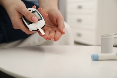 Diabetes. Woman checking blood sugar level with glucometer at light table, closeup