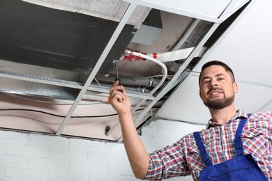 Photo of Professional technician repairing ceiling mounted air conditioner indoors