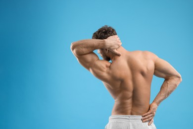 Photo of Man suffering from back and neck pain on light blue background, back view. Space for text