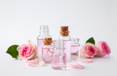 Bottles of essential oil and roses on white background