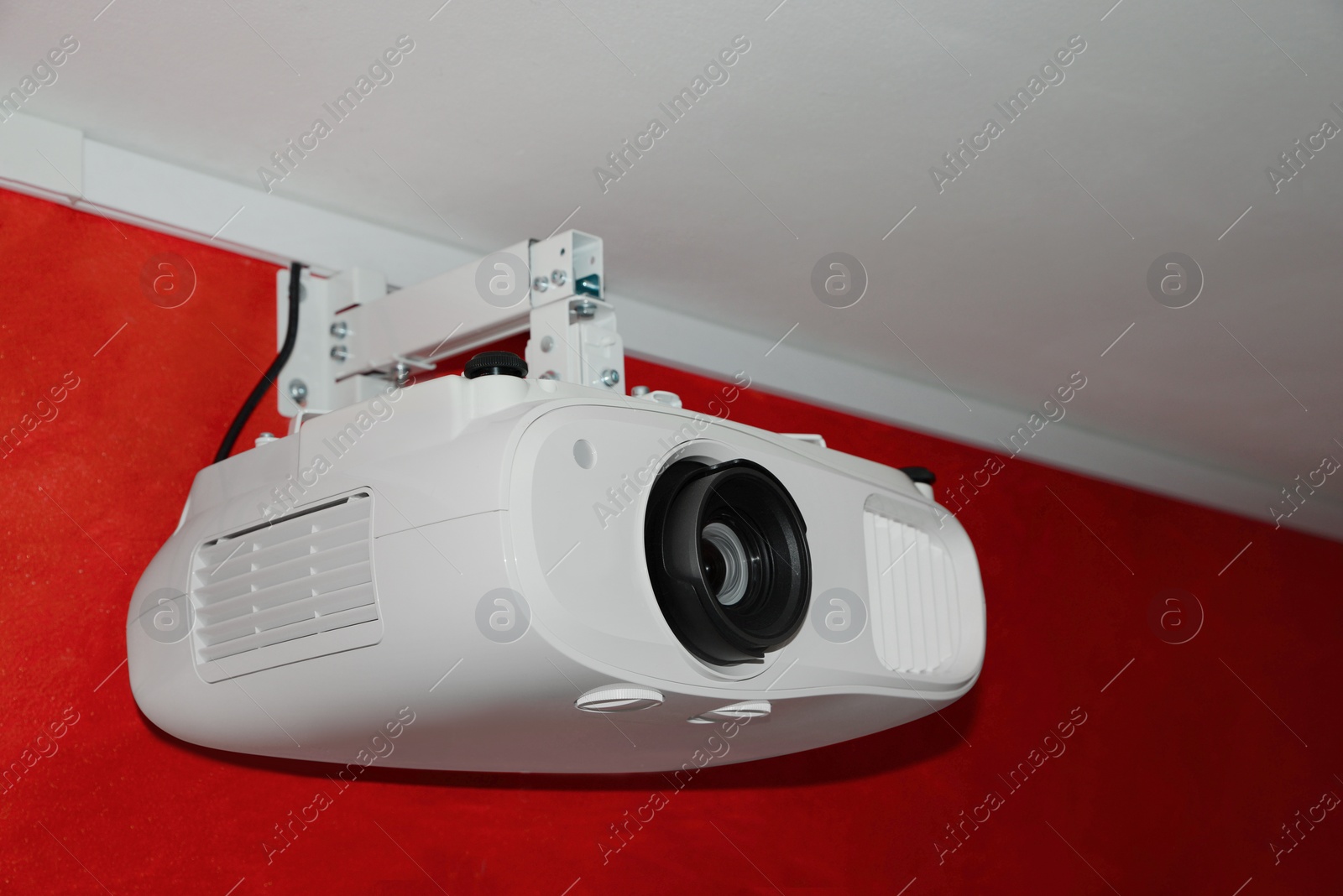 Photo of Modern digital video projector on red wall indoors, closeup