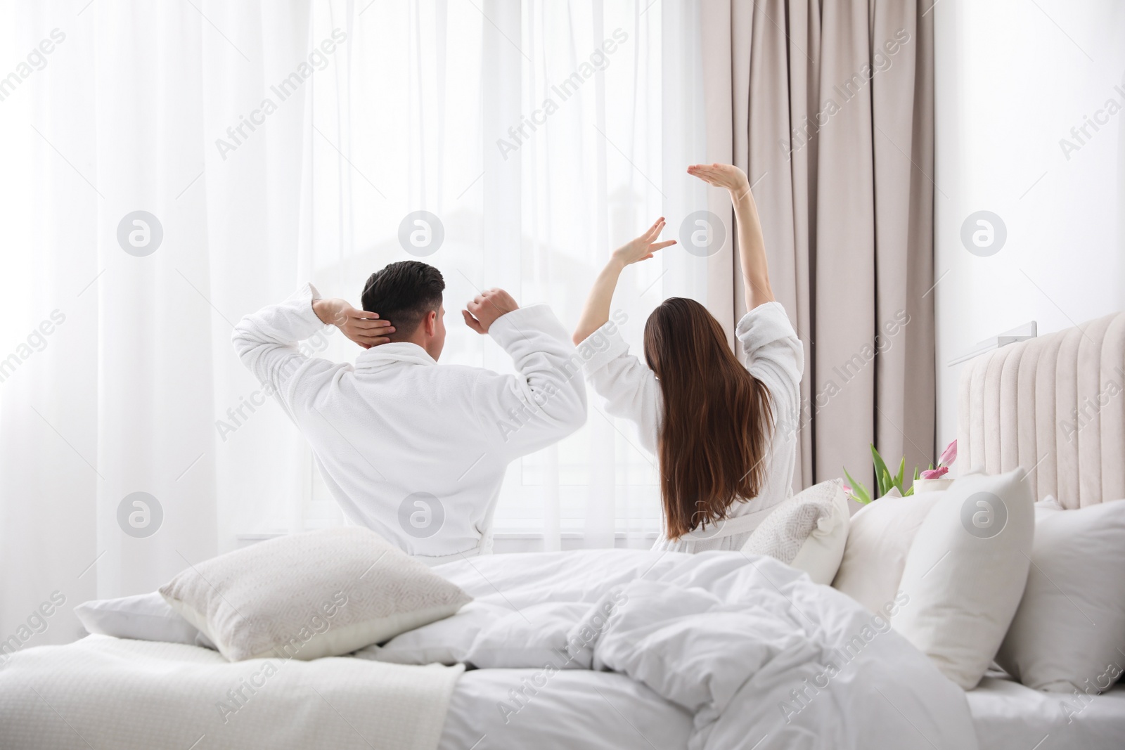 Photo of Happy couple in bathrobes awakening in bedroom