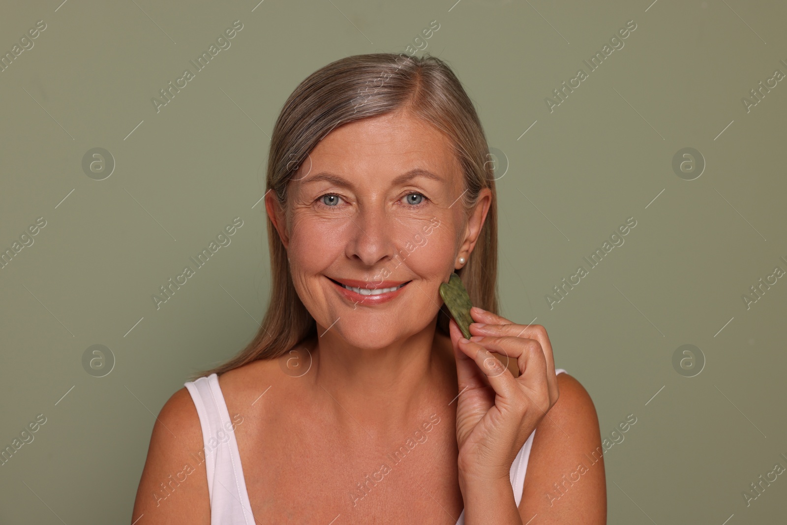 Photo of Woman massaging her face with jade gua sha tool on green background