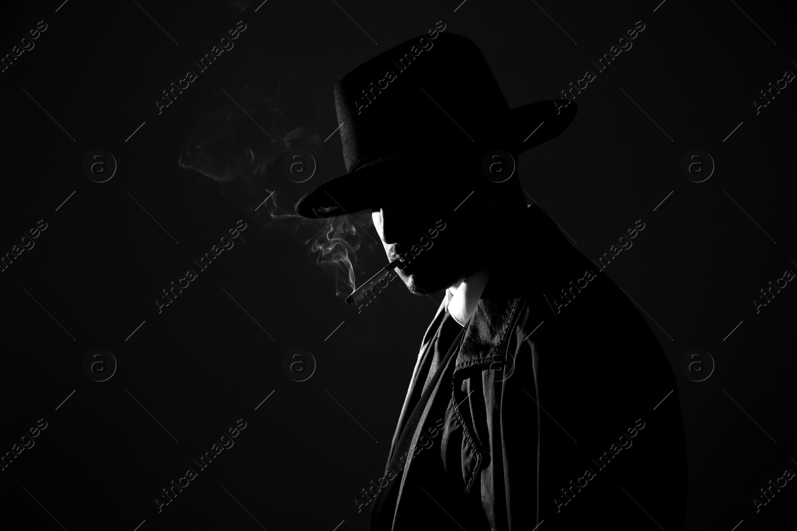 Photo of Old fashioned detective smoking cigarette on dark background, black and white effect