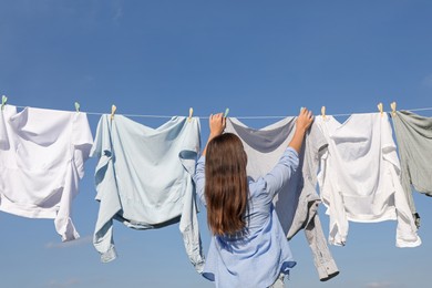 Photo of Woman hanging clothes with clothespins on washing line for drying against blue sky, back view