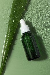 Photo of Bottle of cosmetic product and aloe leaf in water on pale green background, flat lay