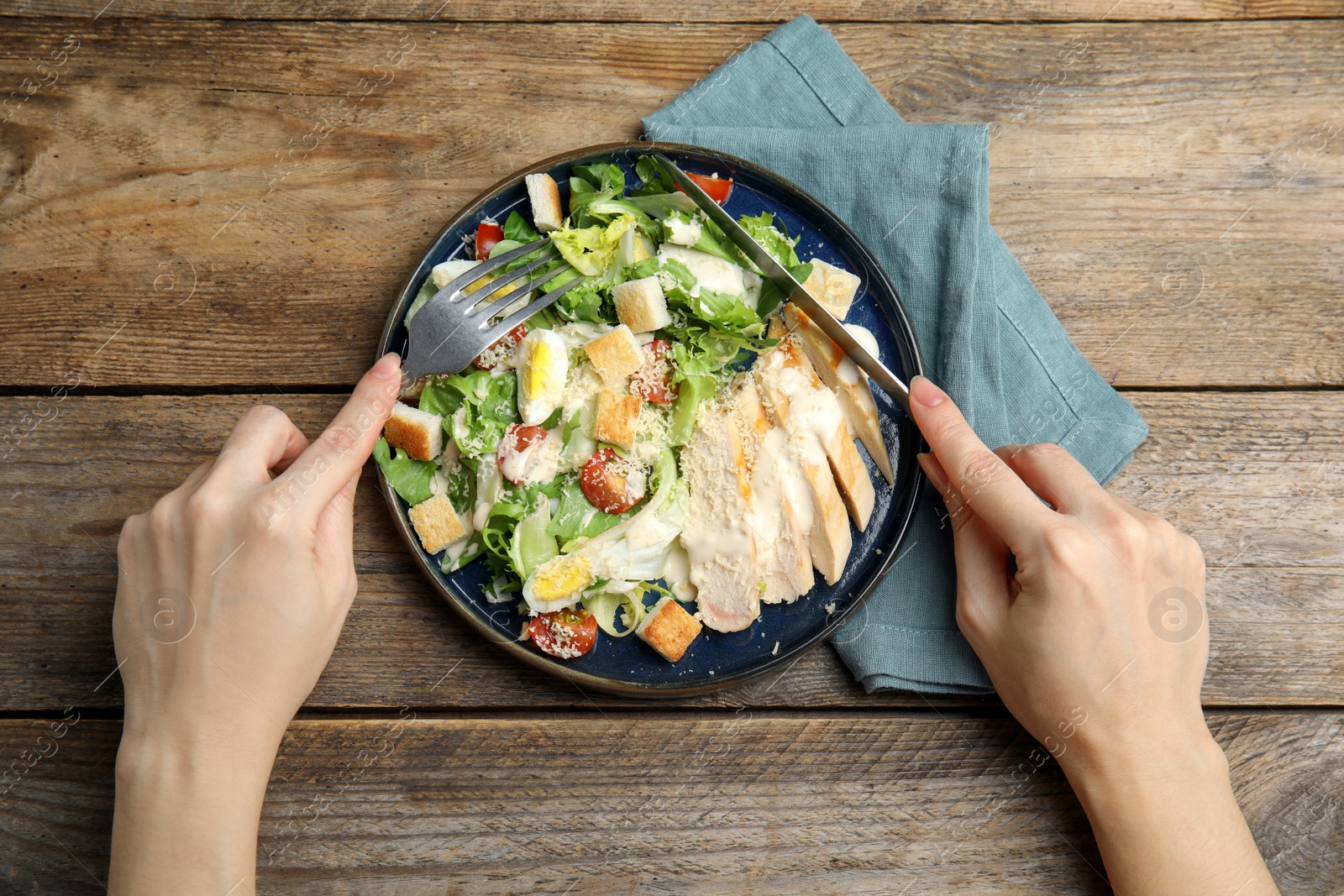 Photo of Woman eating delicious Caesar salad at wooden table, top view