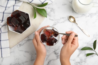 Photo of Woman eating delicious grass jelly cubes at white marble table, top view