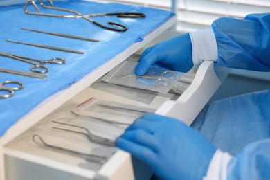 Photo of Doctor putting Pott's scissors into drawer indoors, closeup. Table with different surgical instruments