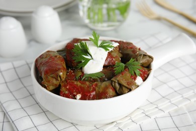 Delicious stuffed grape leaves with sour cream and tomato sauce on table
