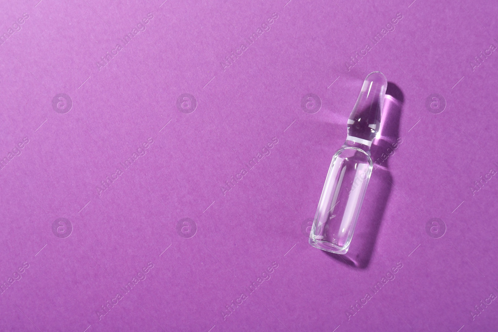 Photo of Glass ampoule with liquid on purple background, top view. Space for text