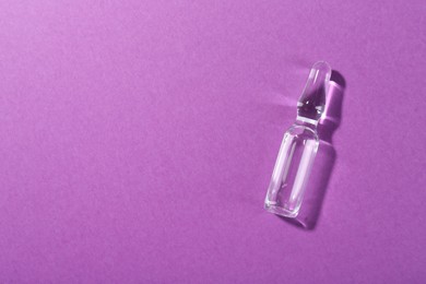 Photo of Glass ampoule with liquid on purple background, top view. Space for text