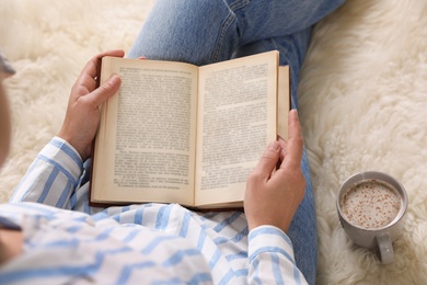 Woman reading book on fuzzy rug, above view