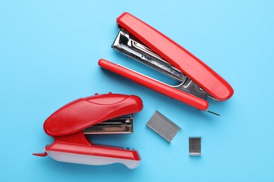 Photo of Bright staplers with staples on light blue background, flat lay