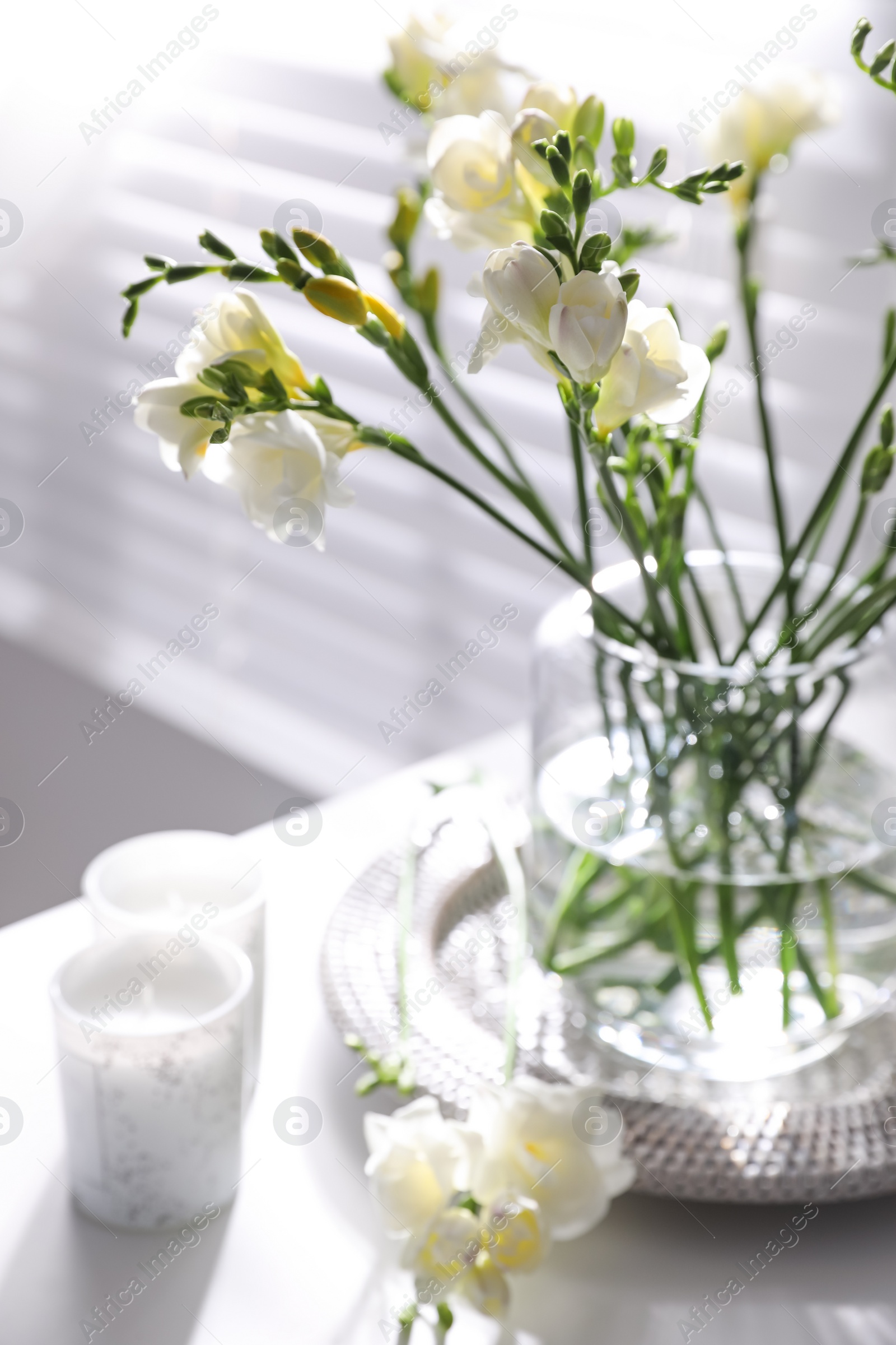 Photo of Beautiful spring freesia flowers and candles on table in room