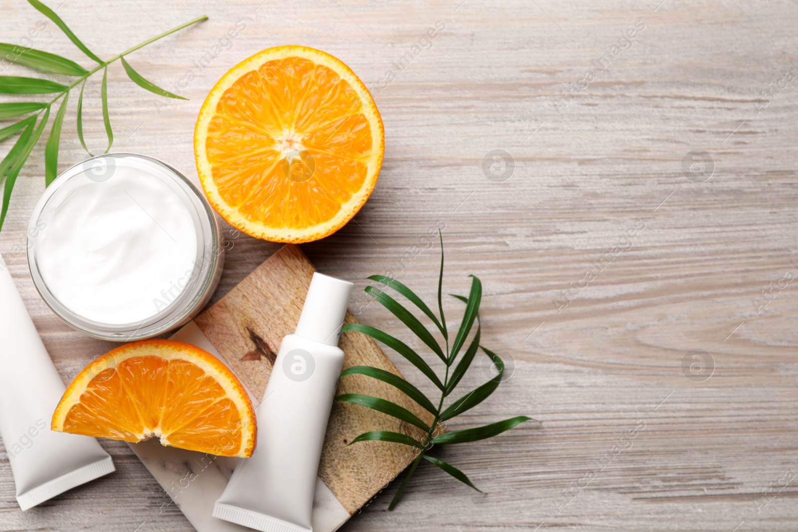 Photo of Different hand care cosmetic products, orange and green leaves on white wooden table, flat lay. Space for text