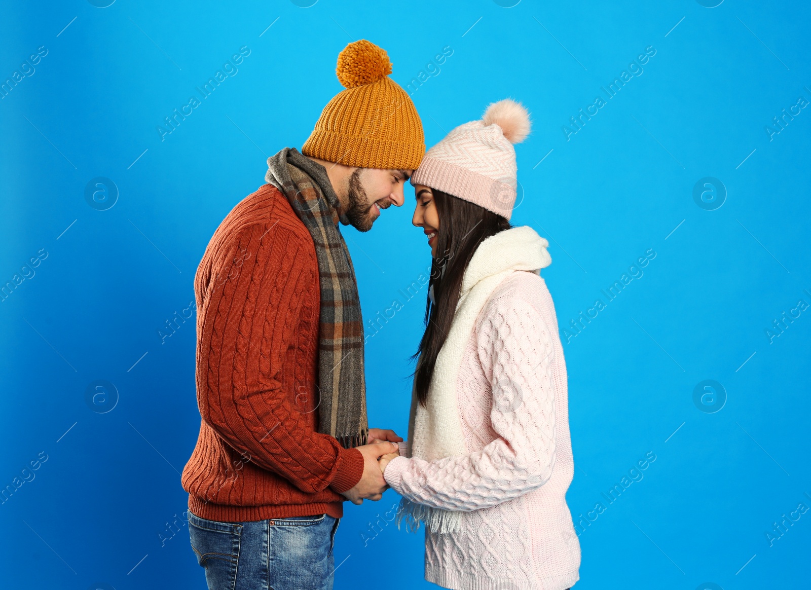 Photo of Happy young couple in warm clothes on blue background. Winter vacation