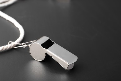 Referee whistle with cord on black table, closeup. Space for text