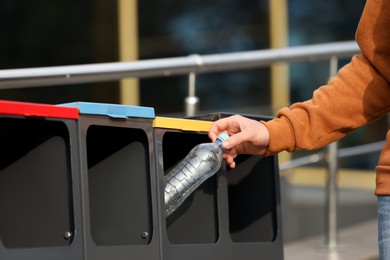 Man throwing plastic bottle into sorting bin outdoors, closeup