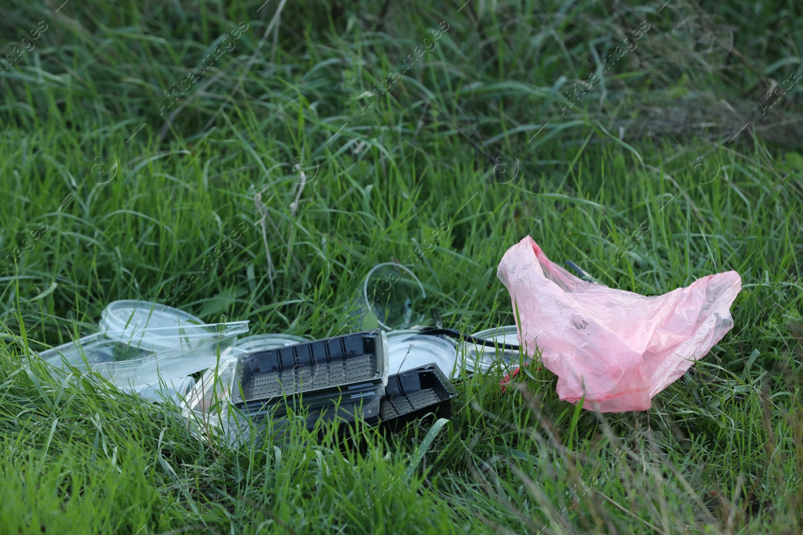 Photo of Used plastic tableware and bag on grass outdoors, space for text. Environmental pollution concept