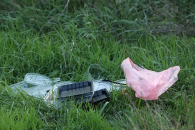 Photo of Used plastic tableware and bag on grass outdoors, space for text. Environmental pollution concept