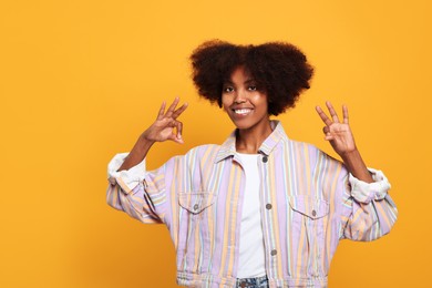 Photo of Smiling African American woman showing ok gesture on orange background. Space for text